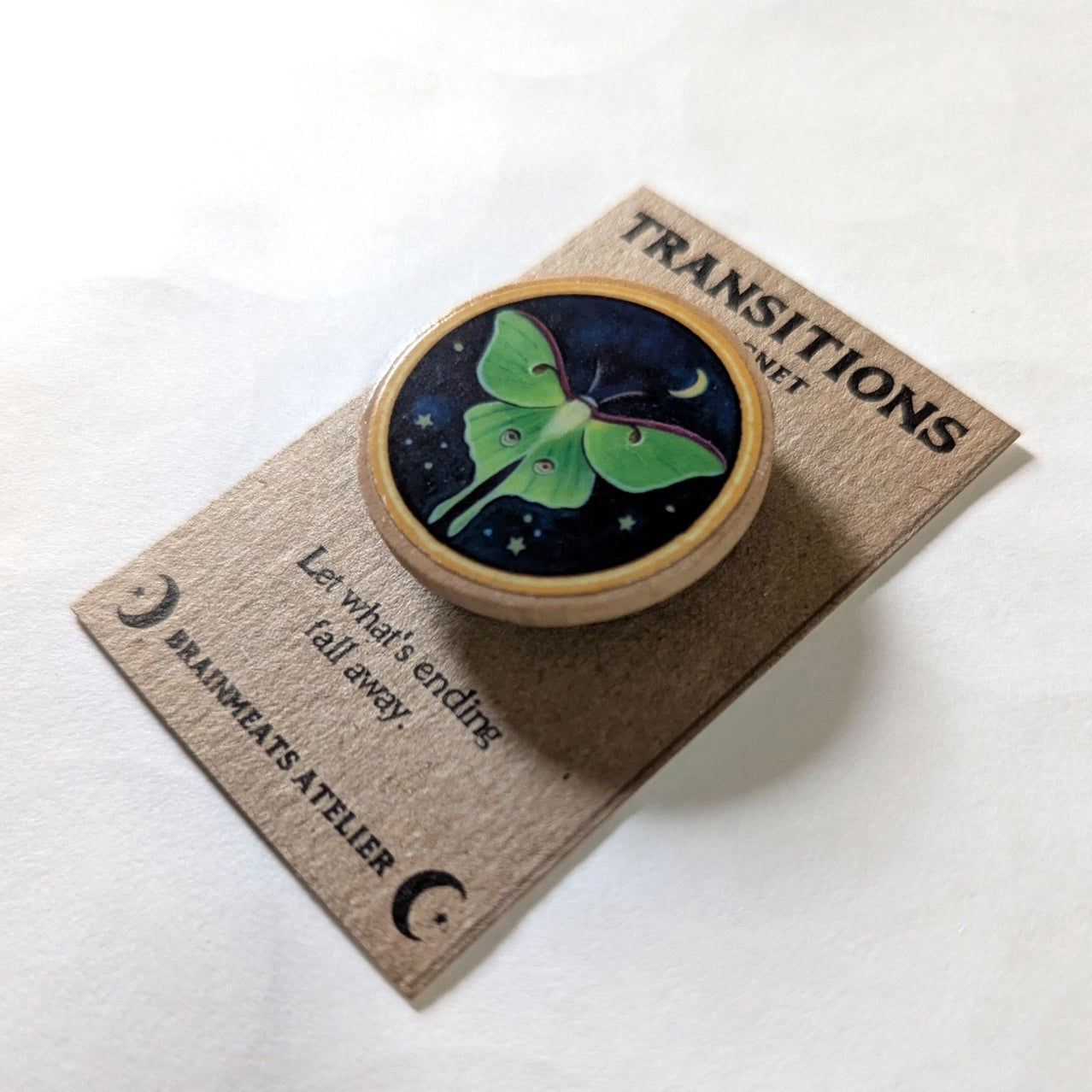 Magnet with butterfly design on a wooden card labeled 'Transitions' by Brainwears Atelier.