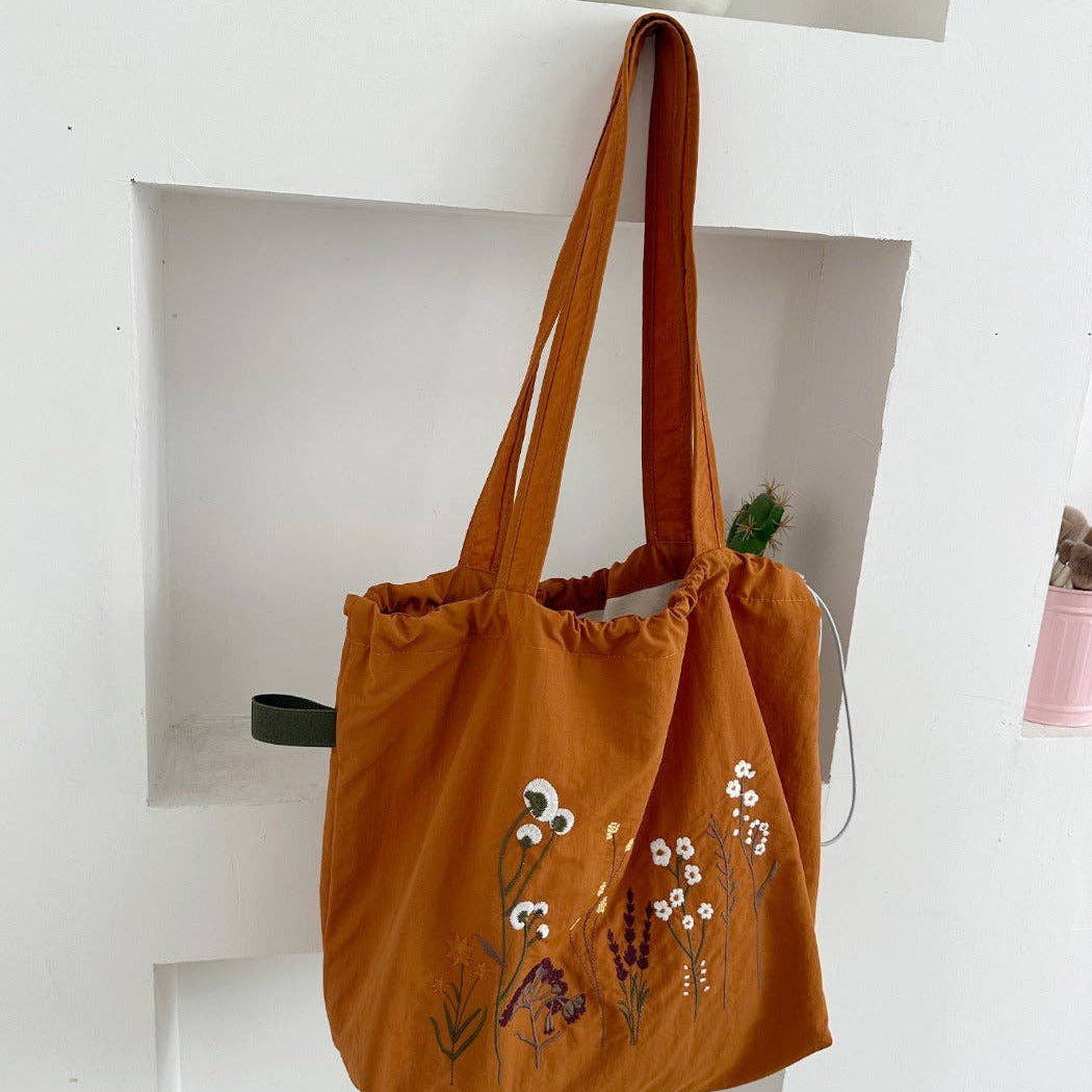 Rust tote bag with floral embroidery on a white shelf