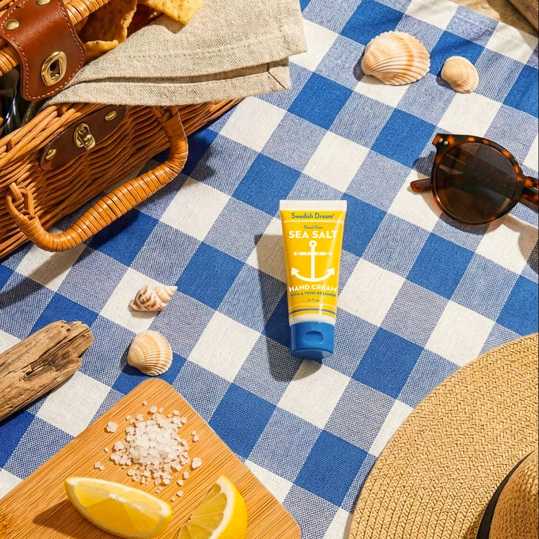 Hand lotion bottle, sunglasses, and other beach items on a blue and white checkered tablecloth.