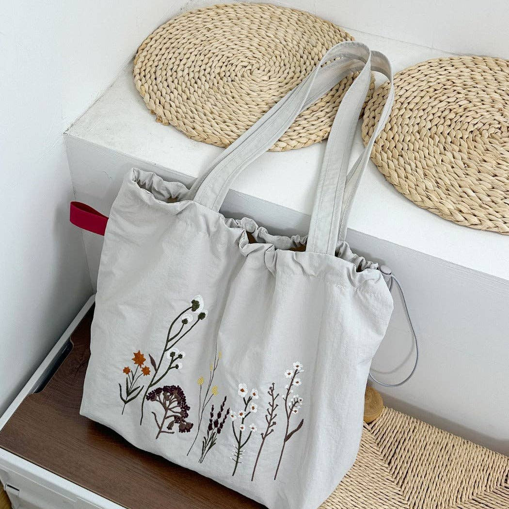 Light Gray tote bag with floral design on a white surface with woven coasters.