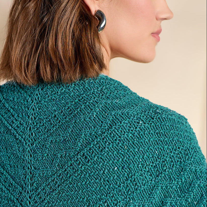 Person wearing a teal knitted shawl on a neutral background