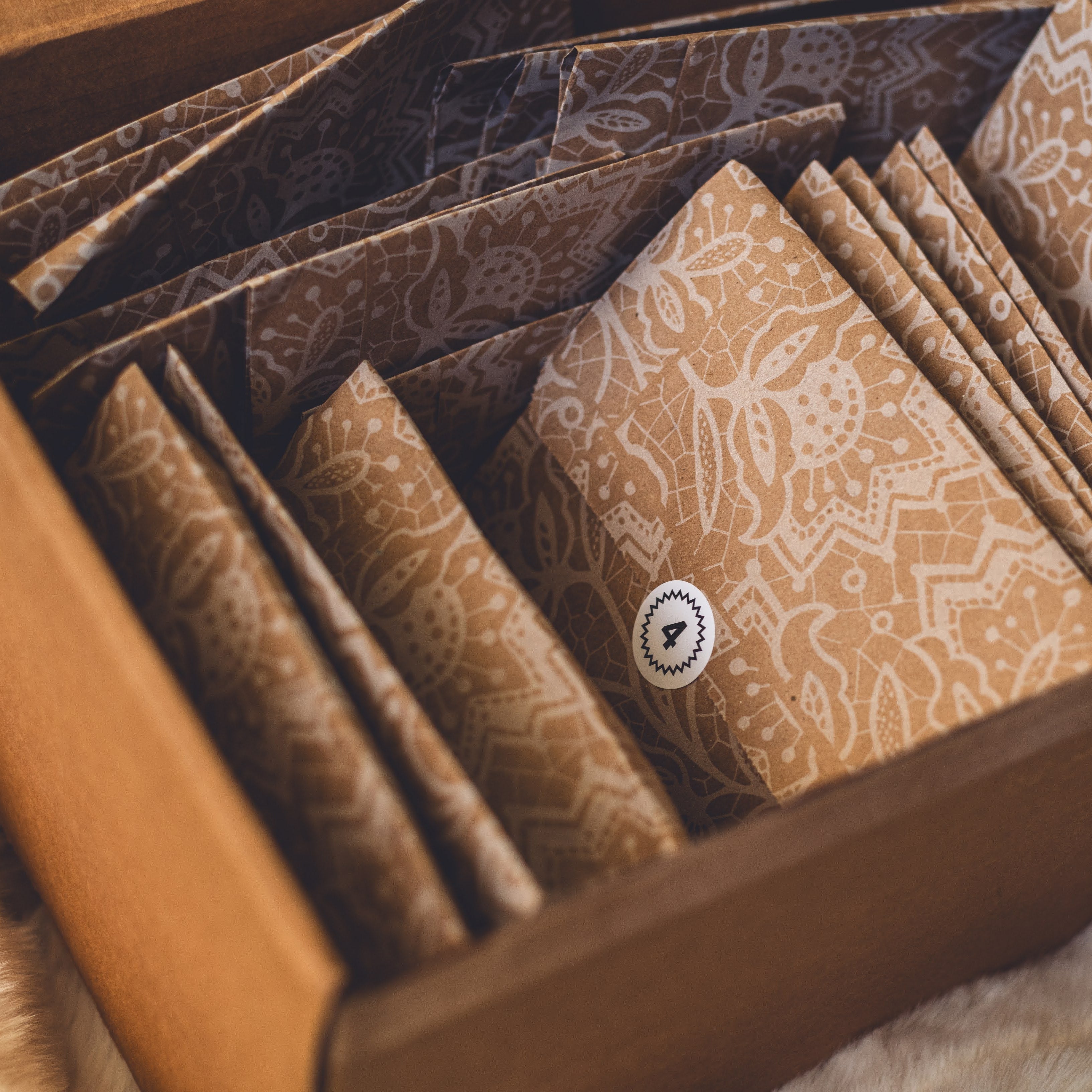 open shipping box revealing 31 kraft paper envelopes with numbered stickers.