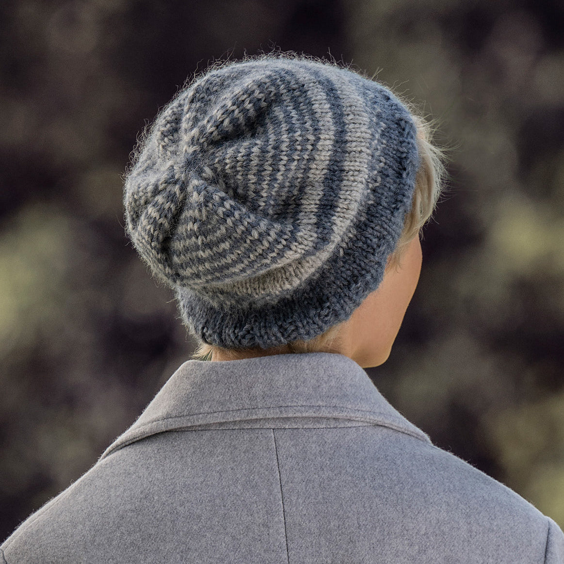 Person wearing a knitted beanie and gray coat with a blurred natural background