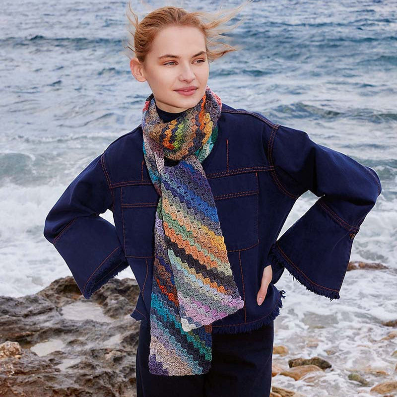 Woman wearing a colorful scarf and navy coat standing on a rocky beach with ocean in the background