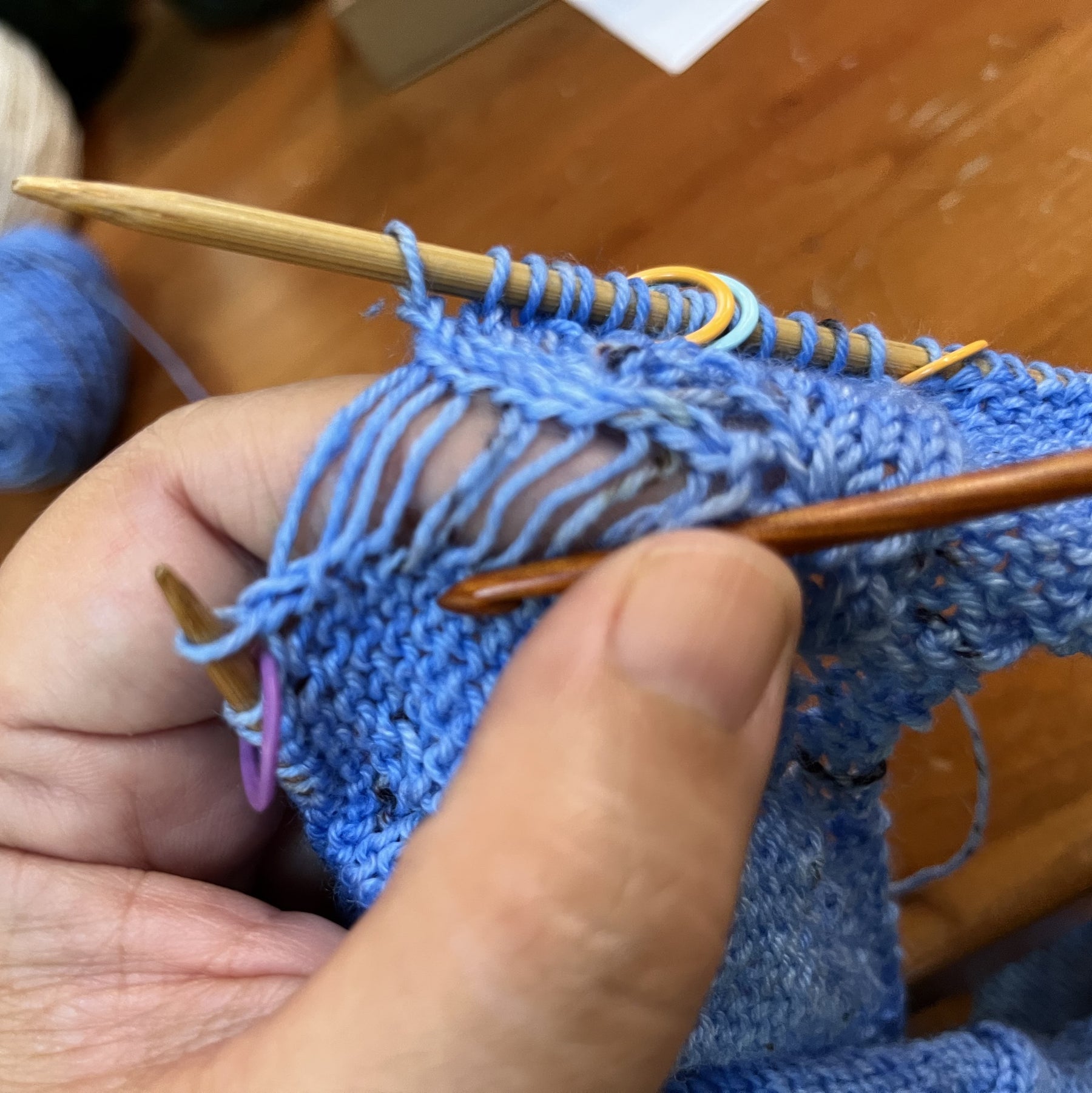 A knitter holds a piece of knitting in her left hand to fix a laddered stitch.