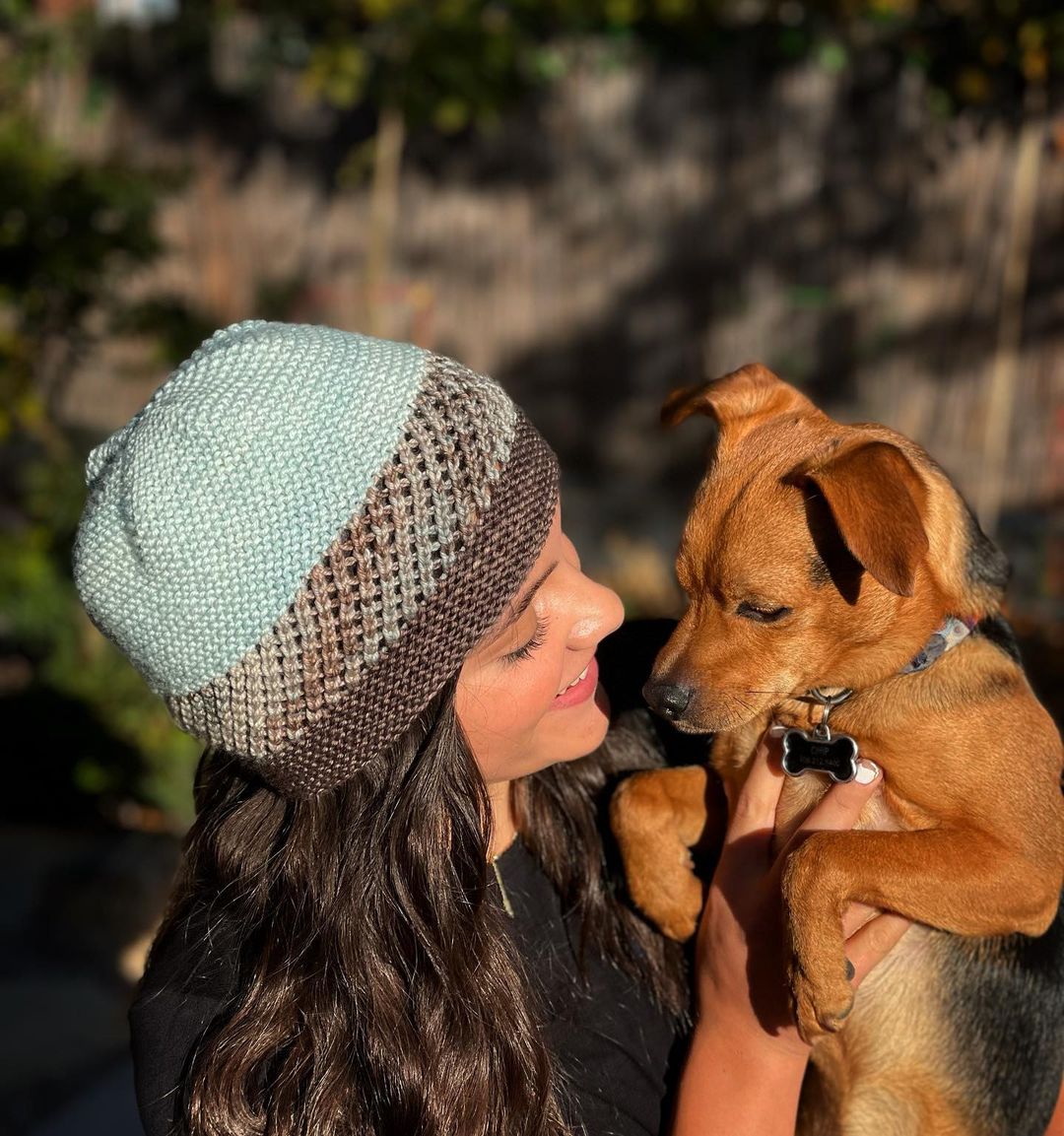 Girl wearing a 3 color knitted hat holding a puppy