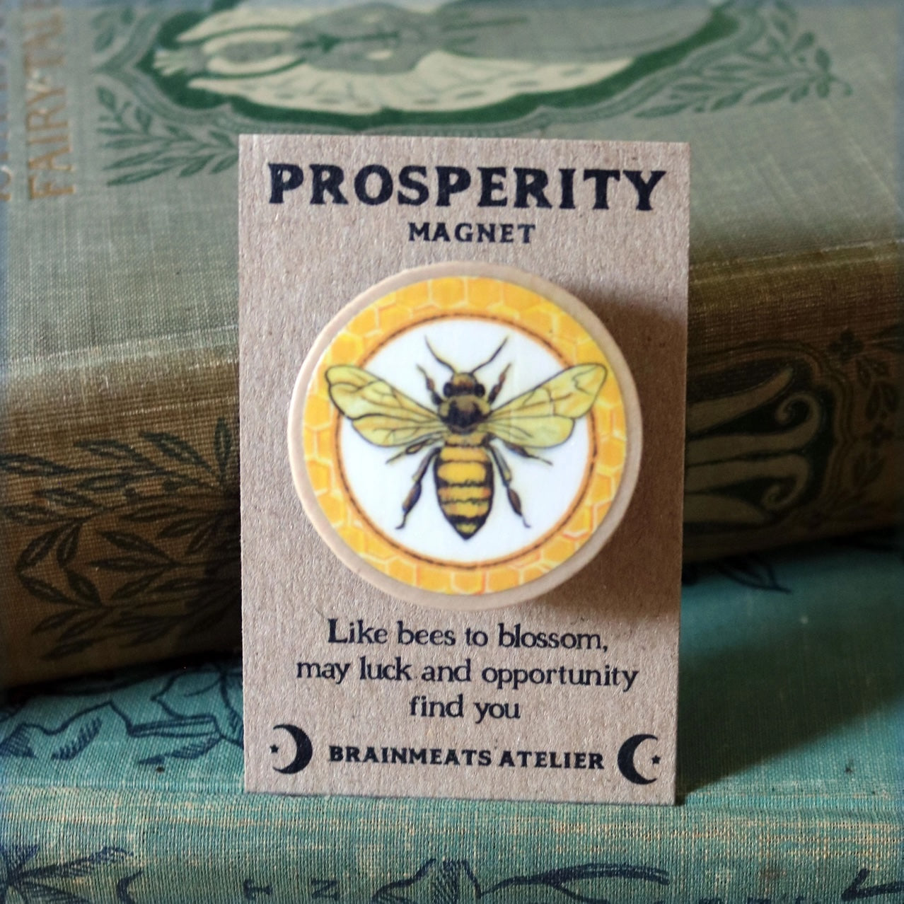 Prosperity magnet with bee illustration on a card, featuring text and branding.