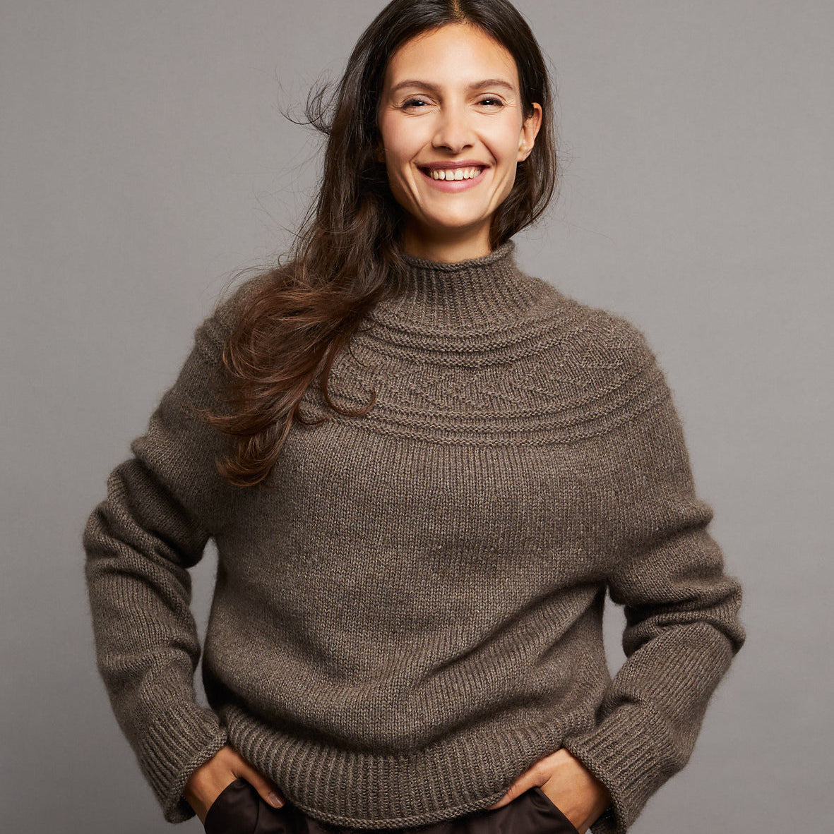 Woman wearing a brown turtleneck sweater against a gray background