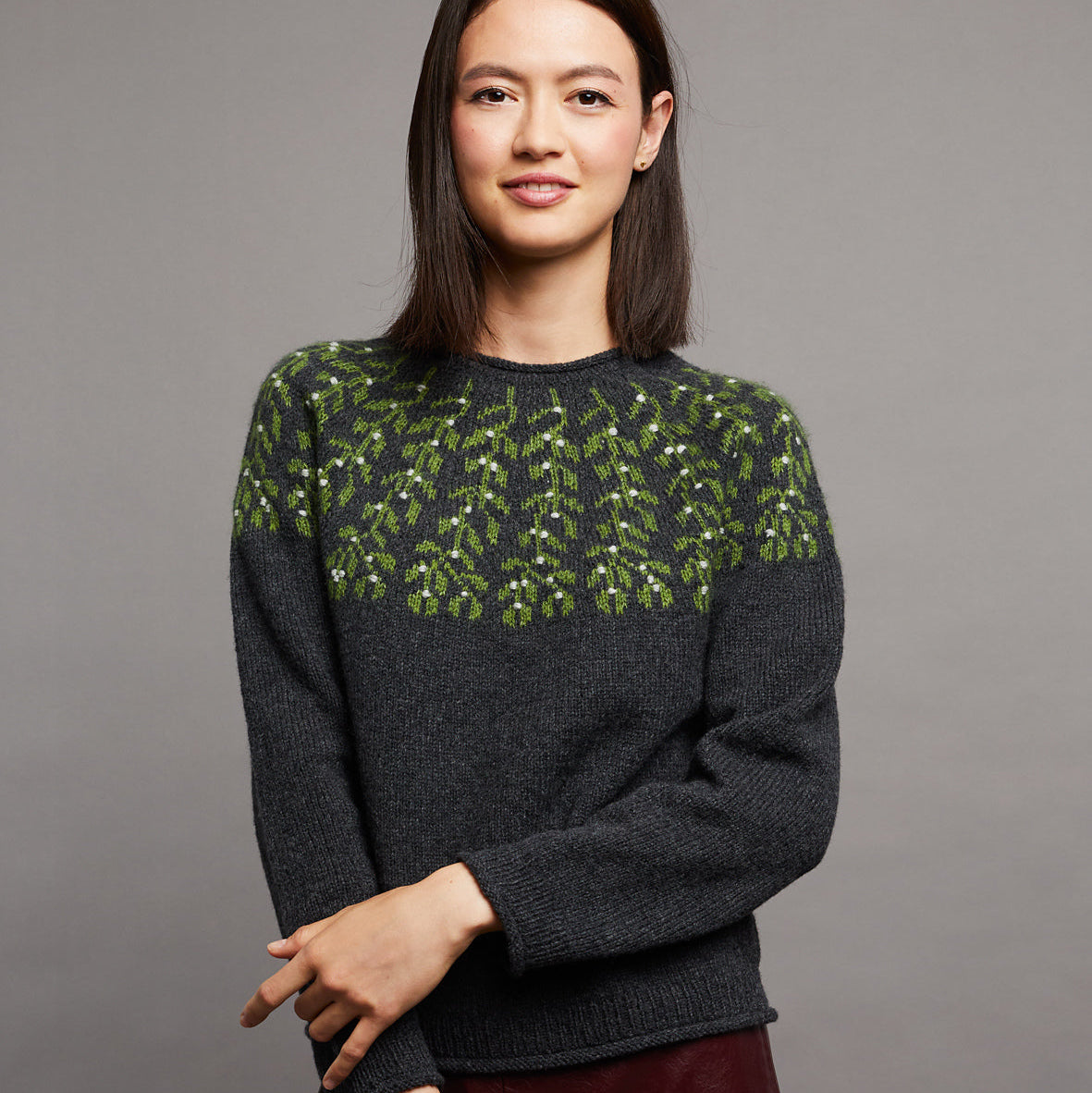 Woman wearing a dark gray sweater with green pattern against a gray background
