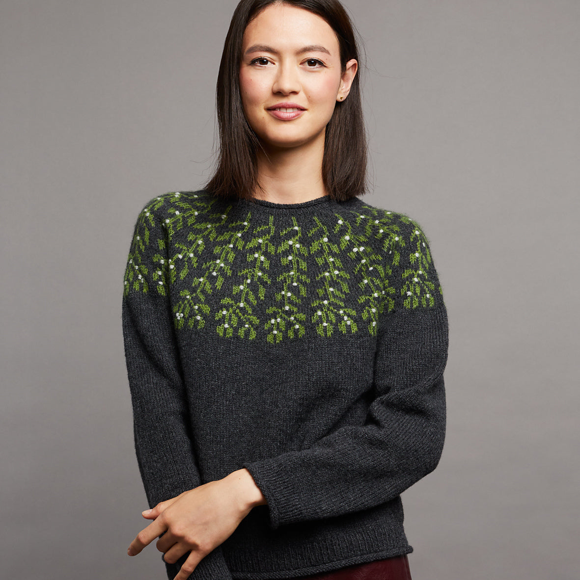 Woman wearing a dark gray sweater with green pattern against a gray background