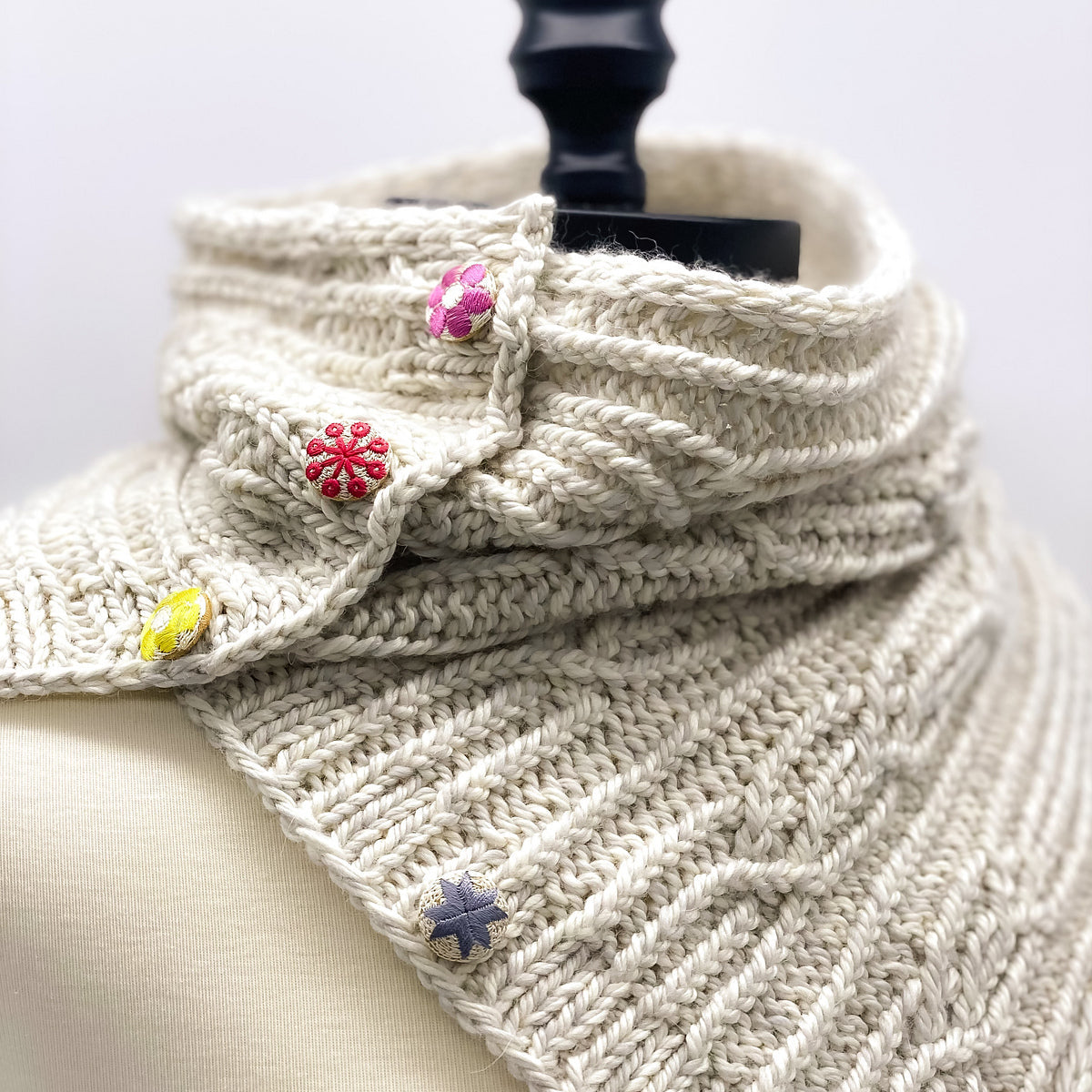 Knitted scarf with colorful buttons on a mannequin against a white background