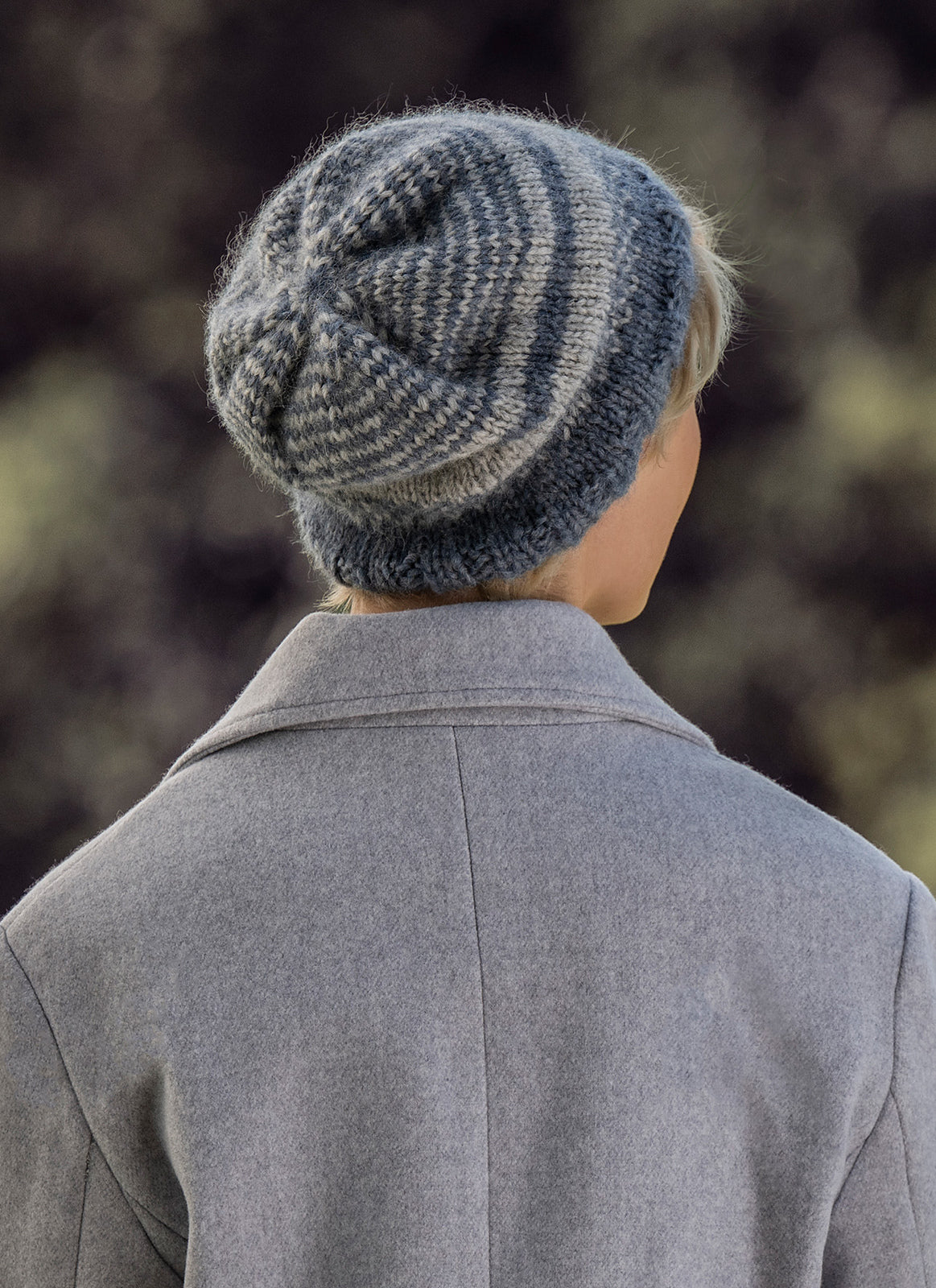 Person wearing a knitted beanie and gray coat with a blurred natural background