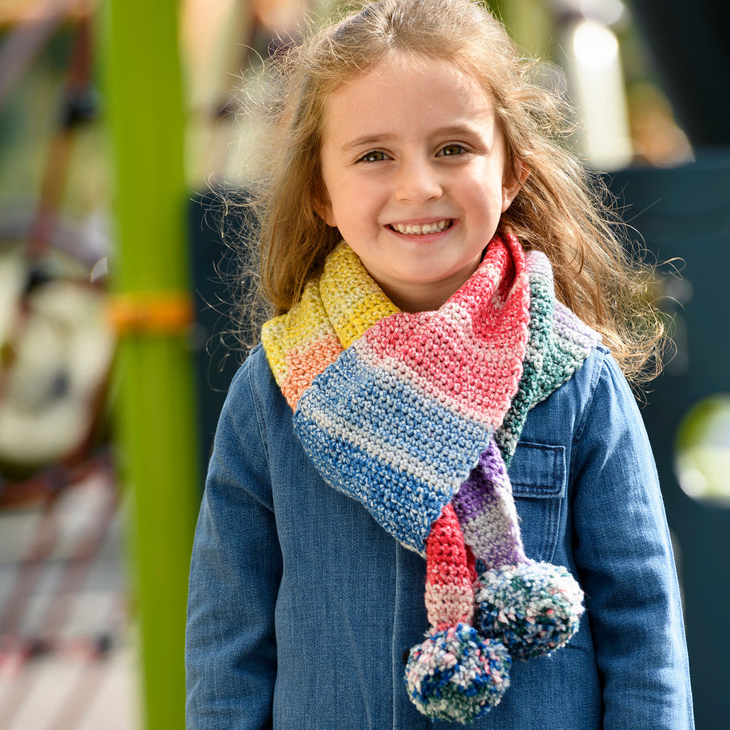 child wearing crocheted scarf with big pom poms