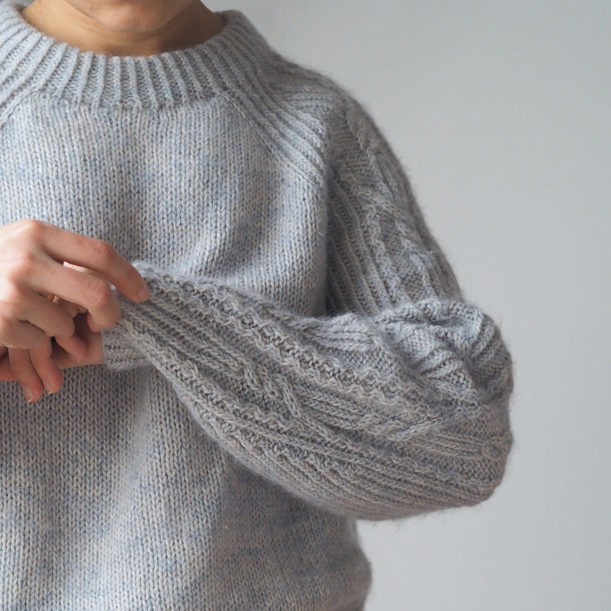 woman wearing a grey raglan sweater with cables on the sleeves