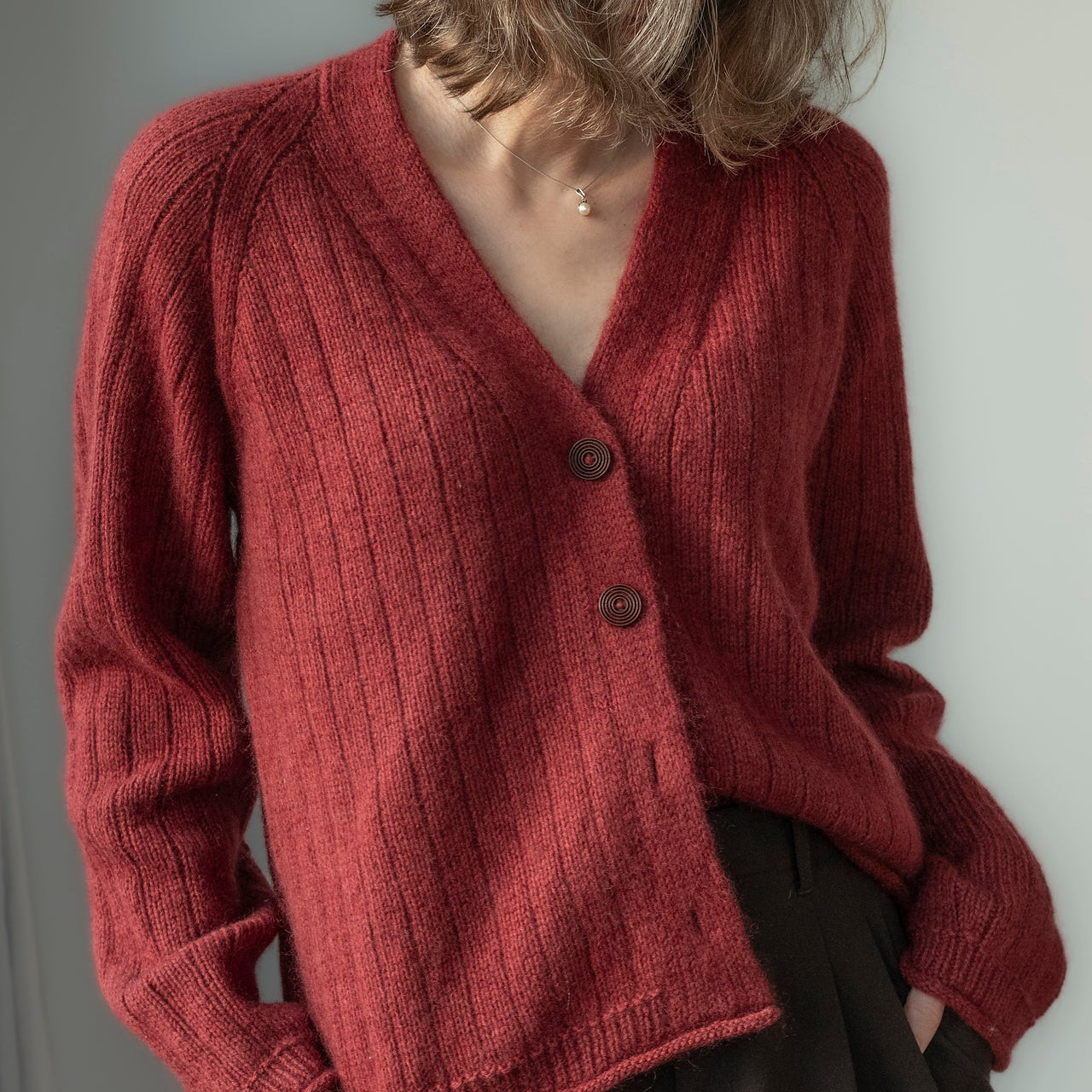 Person wearing a red knitted cardigan against a neutral background